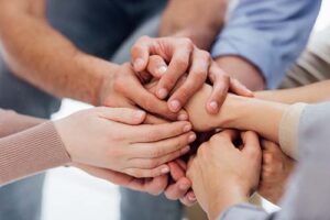 a group of hands joins in a circle of people in an addiction alumni program